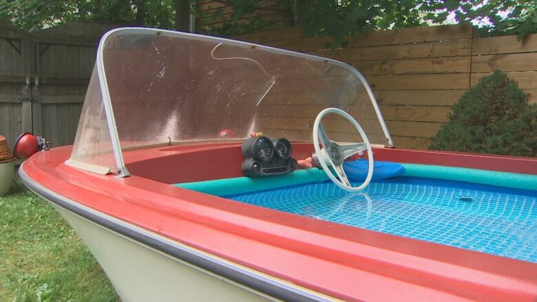 A red boat is seen with its cockpit lined with a pool liner and filled with water