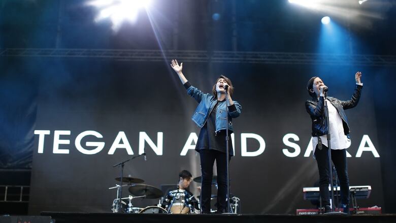 Twins sing on stage with arms outstretched.