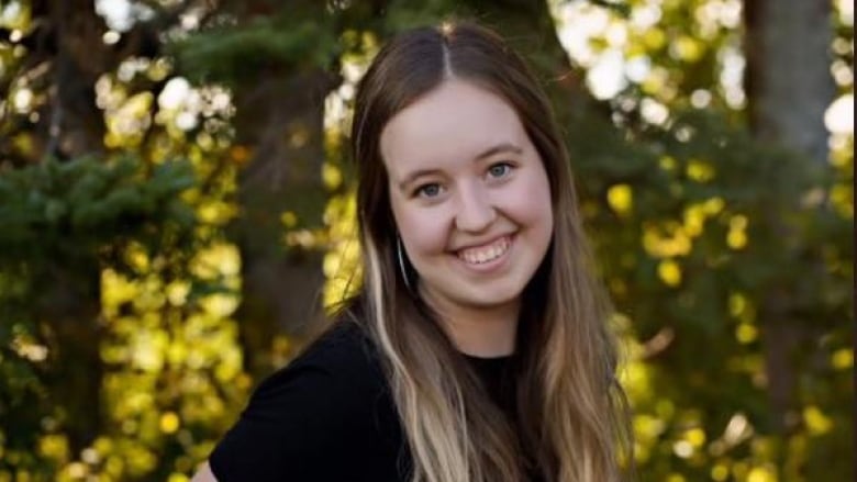 A young woman wearing a black shirt poses in front of trees 