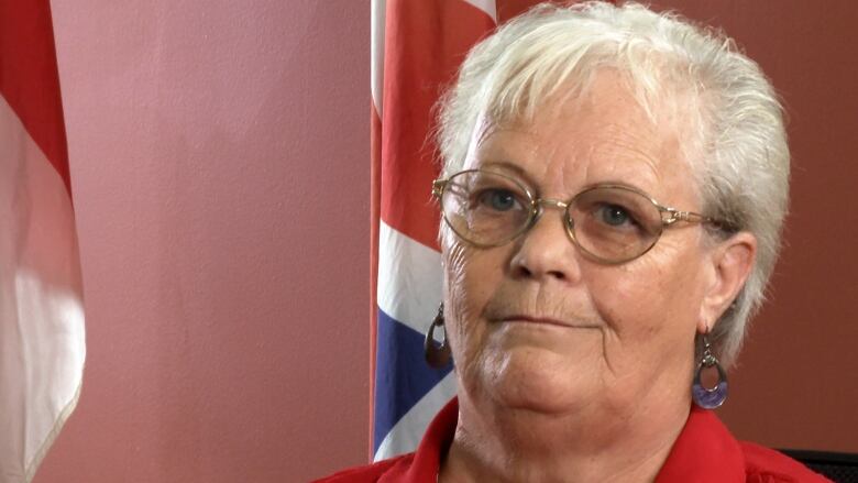 A woman with a red shirt and glasses looks past the camera. 