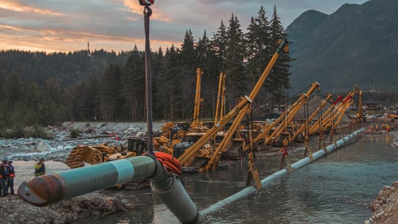 Construction crews can be seen observing work on a pipeline crossing a river.