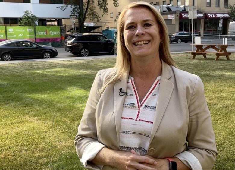 A woman stands in a park, smiling.