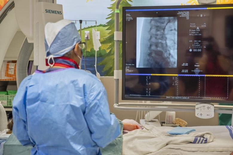 A doctor stands over a child in a hospital room while looking at an image of his spine.