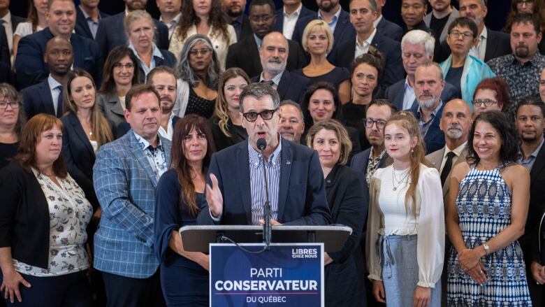 A man speaks into a microphone with people standing behind him