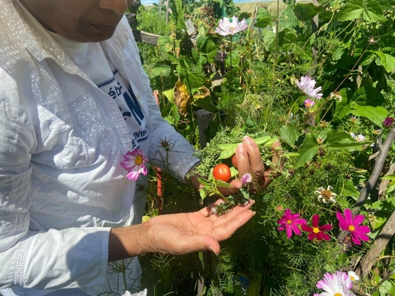 A woman shows off a cherry tomato alongside vibrant purple flowers. 