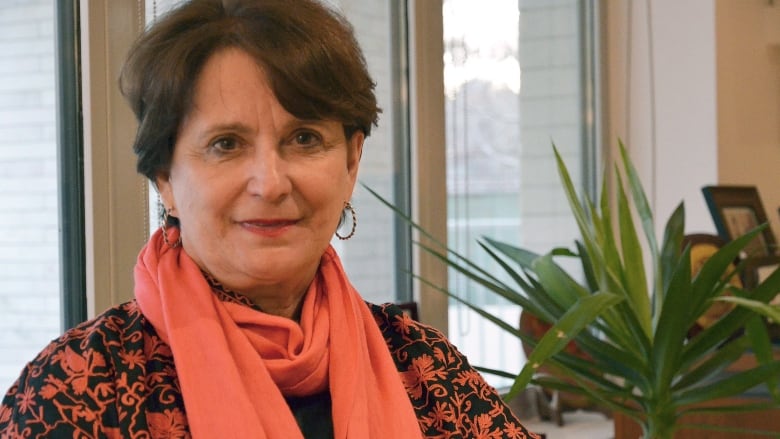 A woman with short brown hair wearing a coral paisley shirt and coral scarf