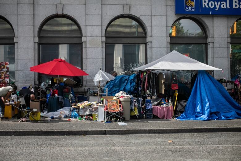 A number of tents, umbrellas, and paraphernalia lie on a pavement in front of a bank.