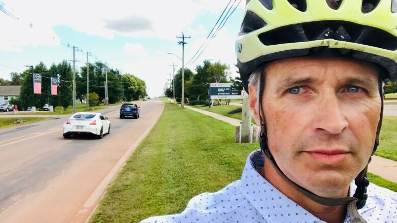 Man in yellow bike helmet with cars going by on street behind him.