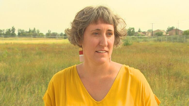 A woman with a bob wearing a yellow shirt stands in a field.