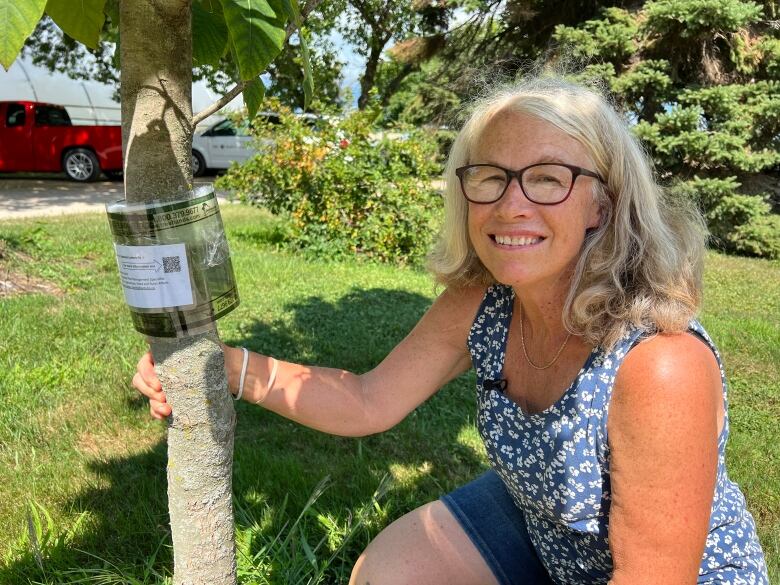 Woman squats next to a small tree with a trap hanging off it.