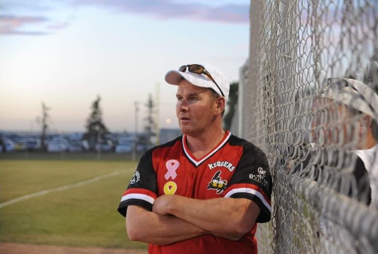 Bert Butler standing on a softball field next to a chain-link fence. 