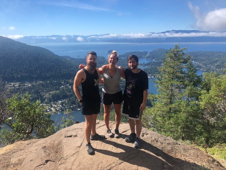 Three people smile as they pose for a picture on a cliff.