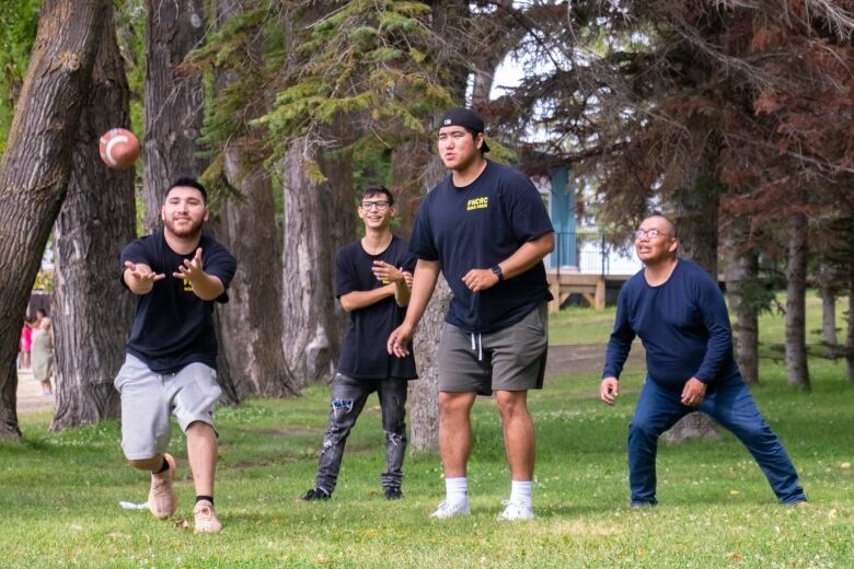 A young man on the right of a group of four reaches out to catch a football.