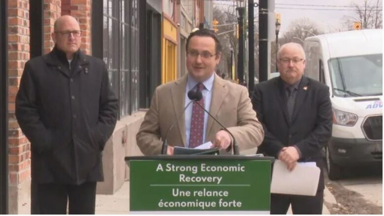 April 1, MP Irek Kusmiercyzk announces a $2.5 million compensation package for businesses impacted by the bridge blockade. He is flanked by Mayor Drew Dilkens and Invest Windsor Essex CEO Stephen MacKenzie. They stand outside the Rock Bottom restaurant in Sandwich Towne. Irek is standing behind a podium that reads A Strong Economic recovery and the same in French.