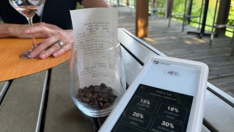 A tip machine asking for tips up to 30 per cent is shown next to an receipt and an empty wine glass held in a woman's hand.