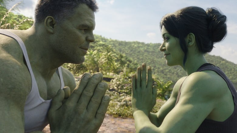 A green-skinned, muscle-bound man and woman face each other in a meditative pose.