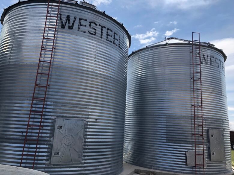 Two large metal storage containers are shown against a blue sky.