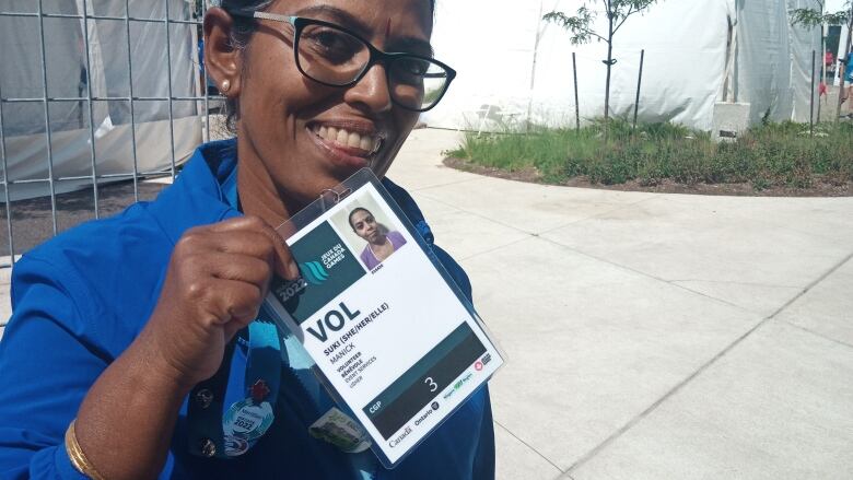 A woman smiles and holds up her volunteer pass. The lanyard attached to it has some pins on it.