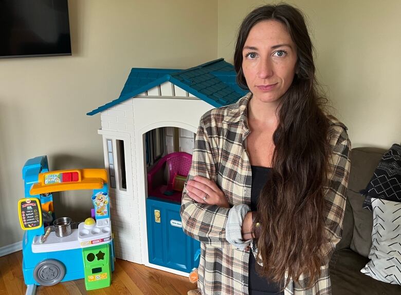 A woman with arms folded, with kids' toys behind her.