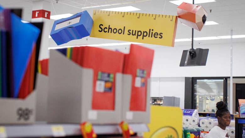 Overhead signage noting school supplies is seen above boxes containing binders, duotangs and other items.