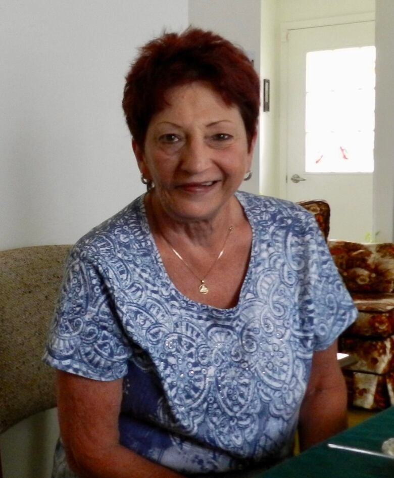 An elderly woman wearing a blue and white shirt smiling at the camera