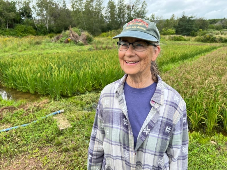 A smiling woman in a green ball cap stands in front of a rice paddy.