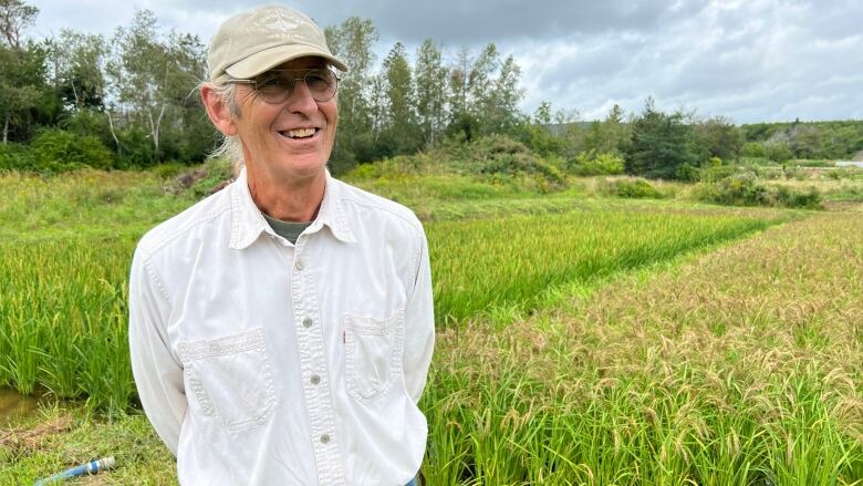 A smiling man in a beige ball cap stands next to a rice paddy.