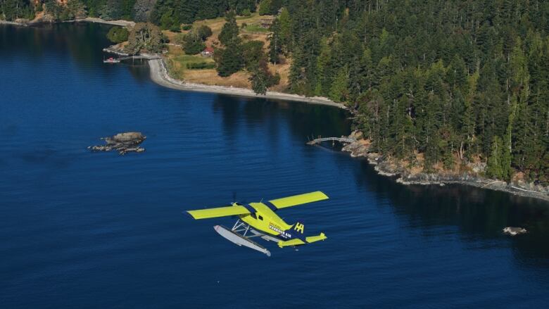 A yellow seaplane flies over a body of water.