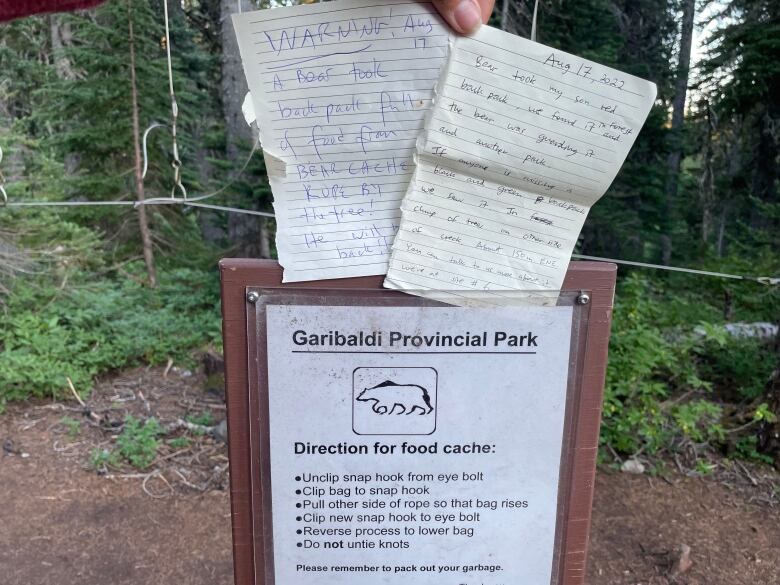 Two notes are hung to a 'Directions for food cache' sign at Garibaldi Provincial Park. One of the notes reads 'WARNING A bear took back pack'.