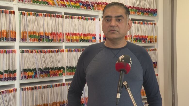 A man stands in front of a wall of files.