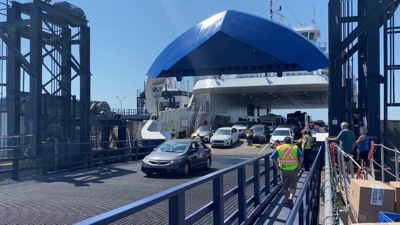 A car drives off a ferry with other cars in the background waiting to disembark.