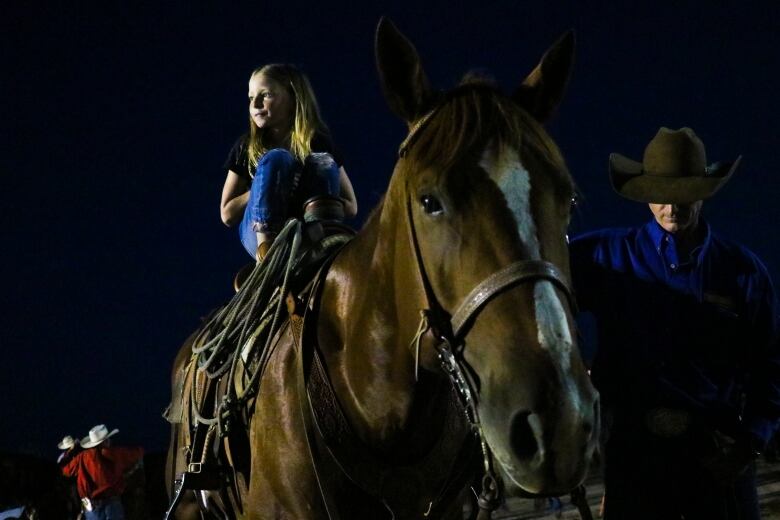 A young child sits on a horse in the dark.