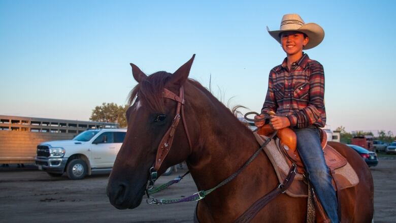 A young girl sits on her horse illuminated by the sunset.