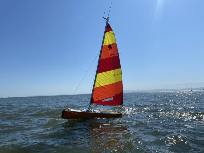 A sailboat on a body of water with red and yellow sails visible.