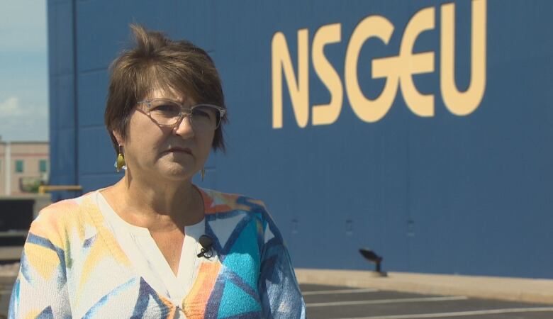 A woman with glasses stands outside in front of a big building.