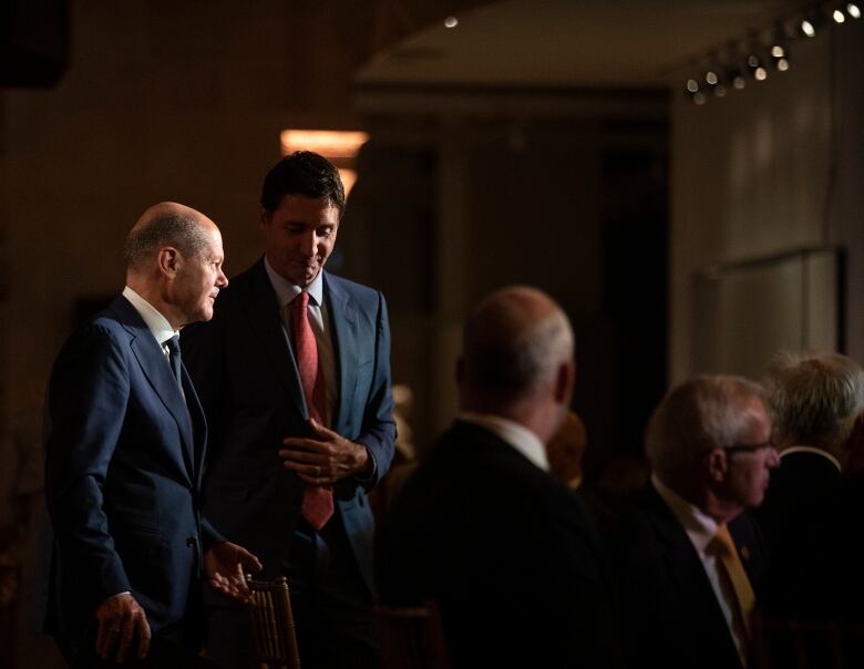 Two men in business suits talk quietly while walking in a banquet hall