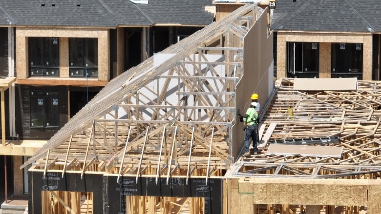 Two men wearing hard hats do work on the frame of a building under construction. 