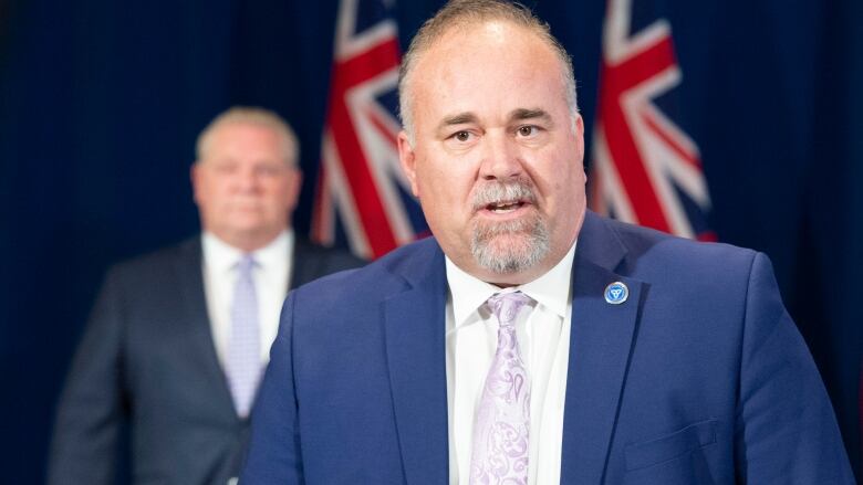 Energy Minister Todd Smith stands at a podium during a news conference while Premier Doug Ford looks on from behind him.