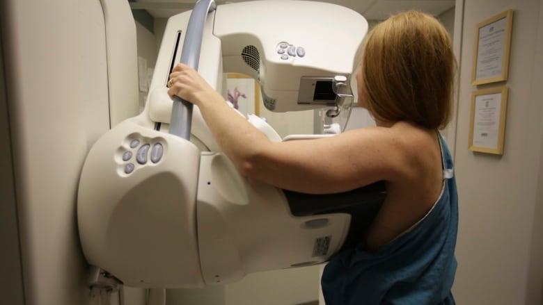 A person, seen from the back, gets a mammogram. The mammography machine is a large, white and grey machine at chest level.