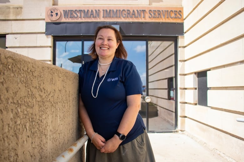 A woman stands outside in front of a sign that says Westman Immigrant Services