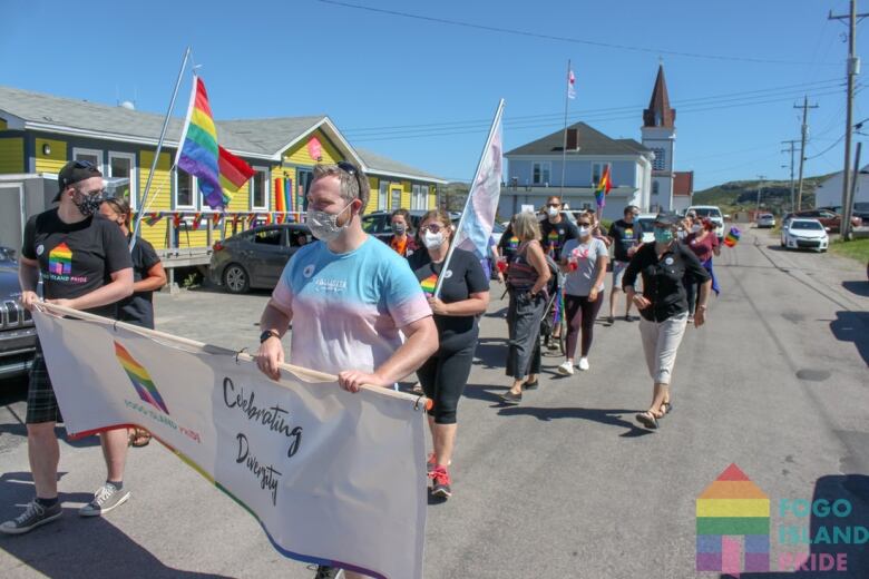 A group carrying rainbow flags and banners march down a town's street.