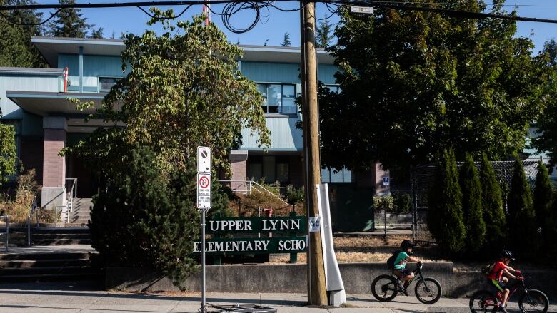 The exterior of Upper Lynn Elementary School, with two children on bikes on the nearby pavement.