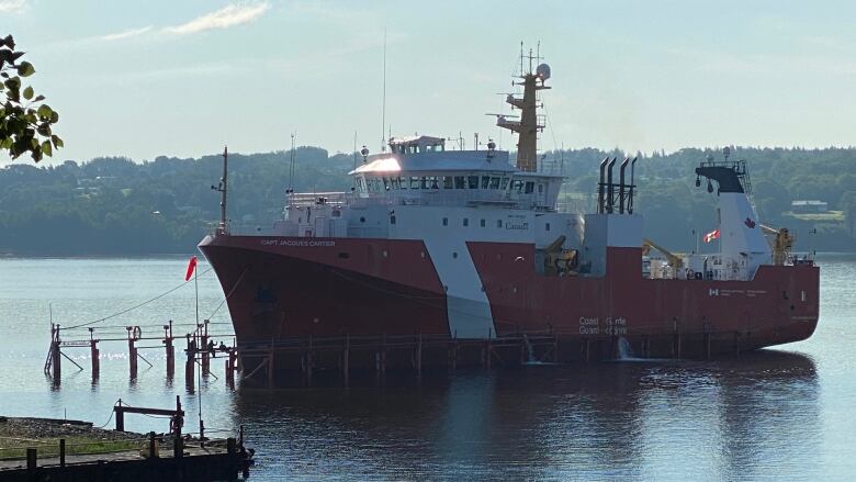 The Canadian Coast Guard offshore fisheries science vessel CCGS Jacques Cartier is seen near a small dock. The hull of the boat is red while the upper portion is white.