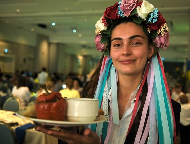 A woman wearing a colourful headress holds a plate of food