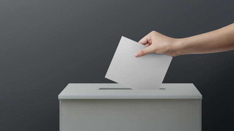 Hand reached out to put white paper into a white ballot box.