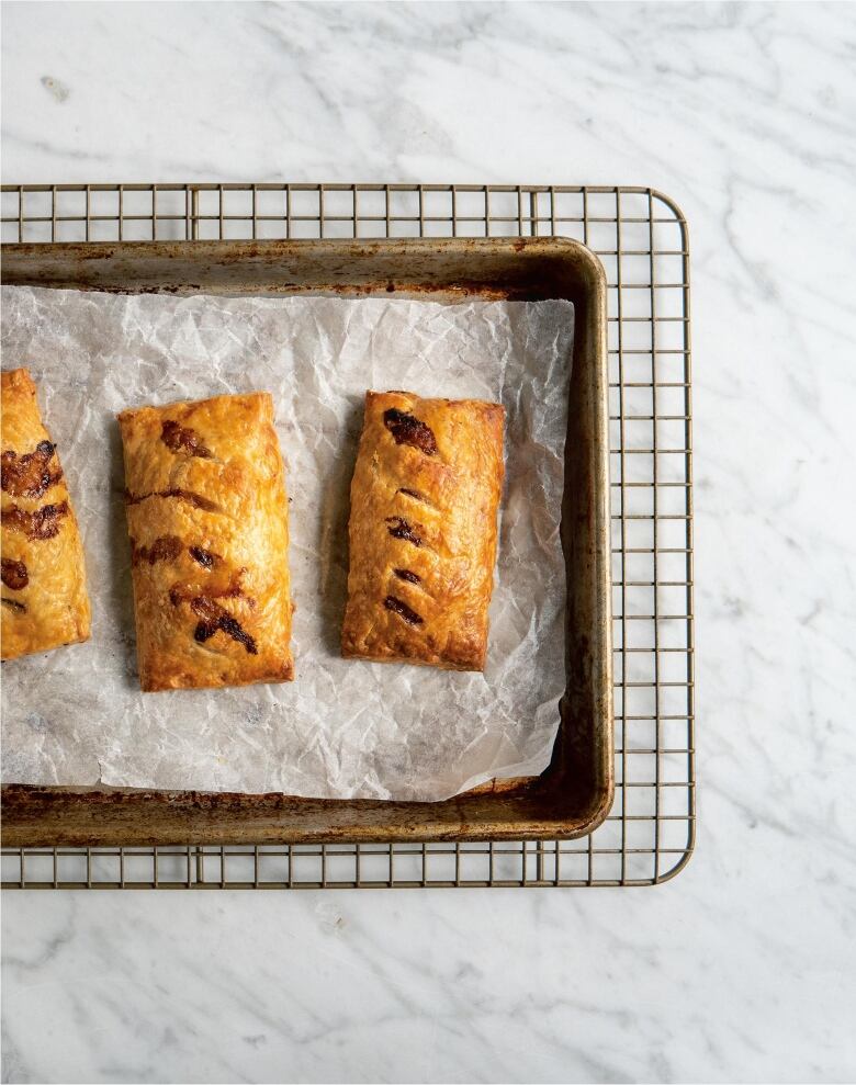 overhead shot of three handpies on a baking sheet, on top of a wire cooling rack, sitting on a marble surface