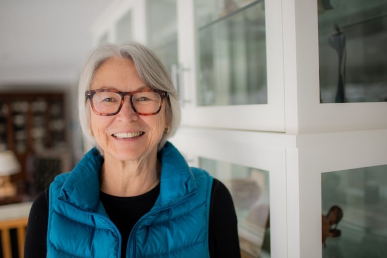 A woman wearing glasses and a bright blue vest smiles