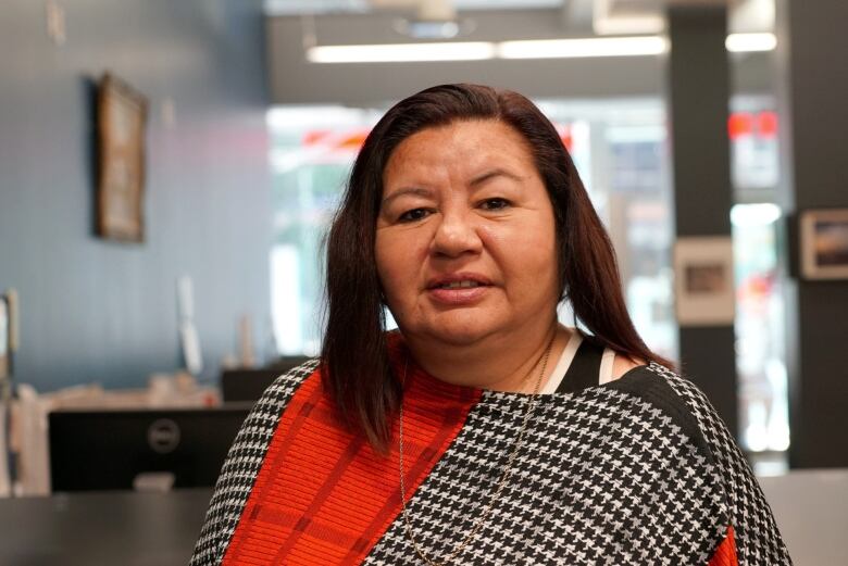 A woman with a red and black shawl poses for a photo in an office.