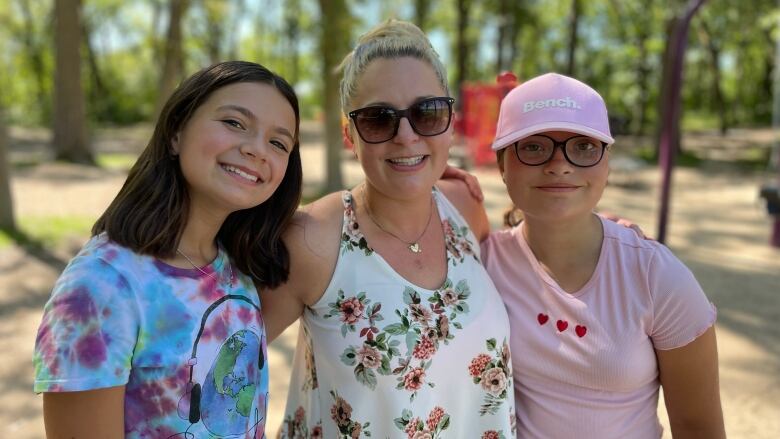 A woman stands smiling with her arms around two girls.