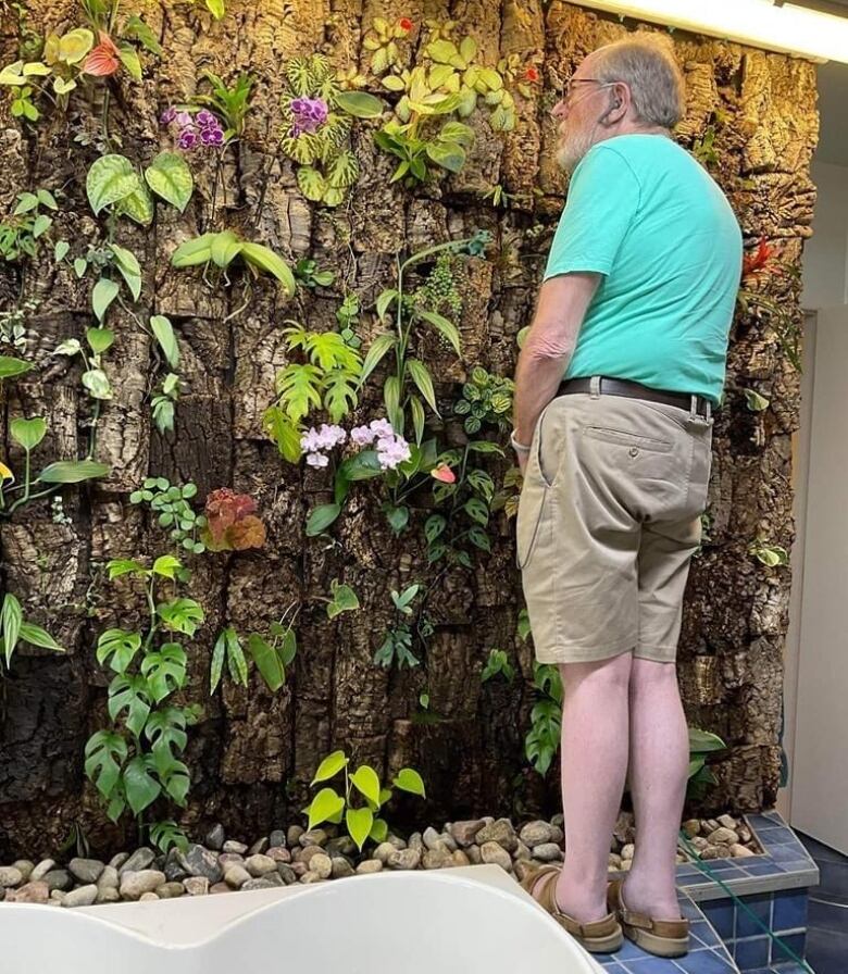 A man stands in front of a wall full of plants and flowers.